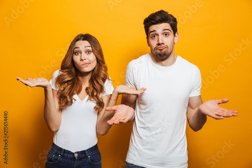 Image of happy young people man and woman in basic clothing throwing up arms with puzzlement, isolated over yellow background