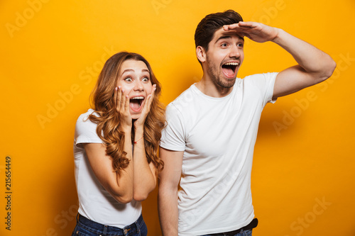 Image of delighted man and woman 20s in basic clothing screaming in surprise and looking aside with hand at forehead, isolated over yellow background