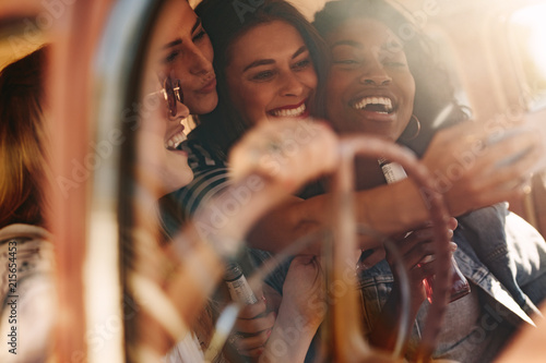 Female friends taking selfie with in the car. Group of women having fun on the road trip taking self portrait with mobile phone.