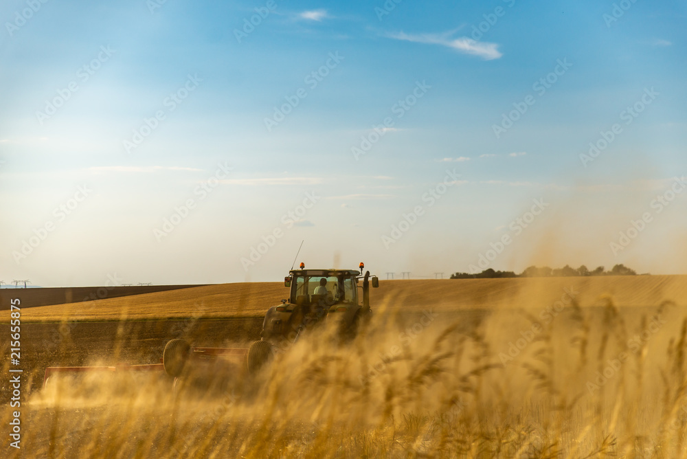 Fototapeta premium Le fermier sur son tracteur agricole prépare sa terre pour aérer les sols en formant de la fumée de poussière