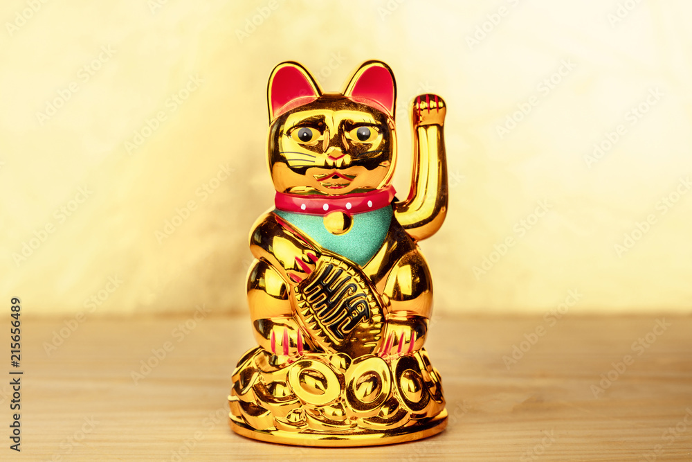 Fototapeta premium Maneki neko, japońska figurka kota, przywołująca szczęście, na złotym tle z miejsca na kopię