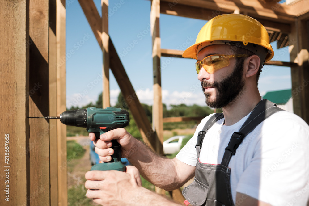 The man is a builder on the roof of a wooden frame house.