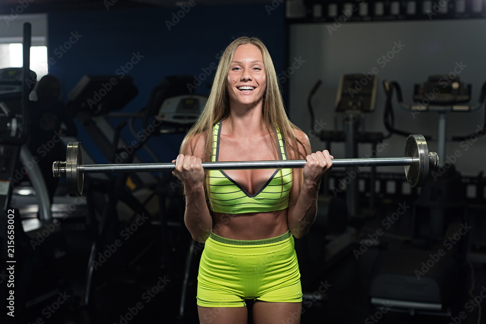 Beautiful sexy athletic muscular young girl. Fitness girl trains in the gym, doing exercises with a barbell Beautiful sexy athletic muscular young girl. Fitness girl trains in the gym, doing exercises with a barbell