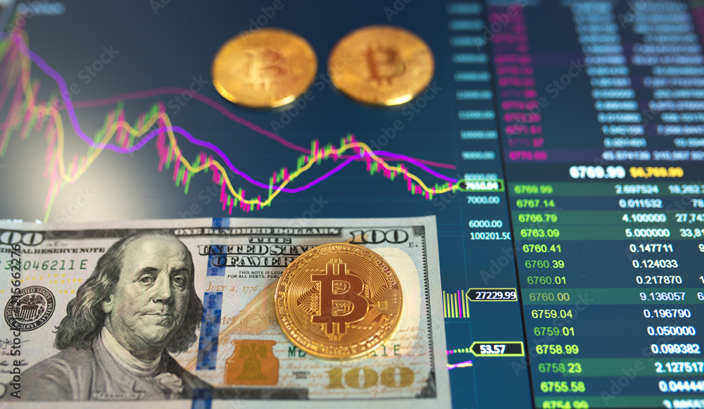 Fototapeta premium Paper bill hundred Dollar, USD, blurred background. The electronic schedule of bitcoin on the exchange, volume trades, on the monitor lie gold coins bitcoin.
