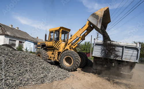 Yellow loader delivering stone gravel into truck during road construction works. The stones for the road. Unloading stone.