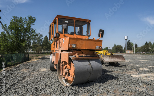 Orange light Vibration roller compactor standing on a stones at road construction and repairing asphalt pavement works with a blue sky. photo