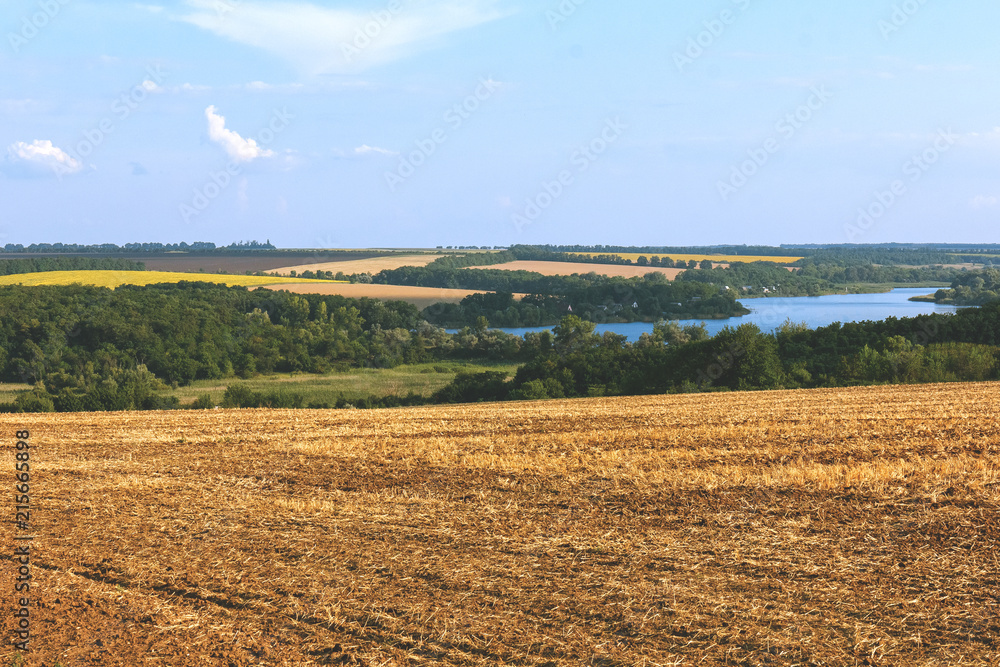 Countryside landscape with fields under blue sky with clouds on sunny day.