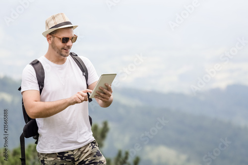Portrait of young traveler with backpack holding and looking at digital tablet device.