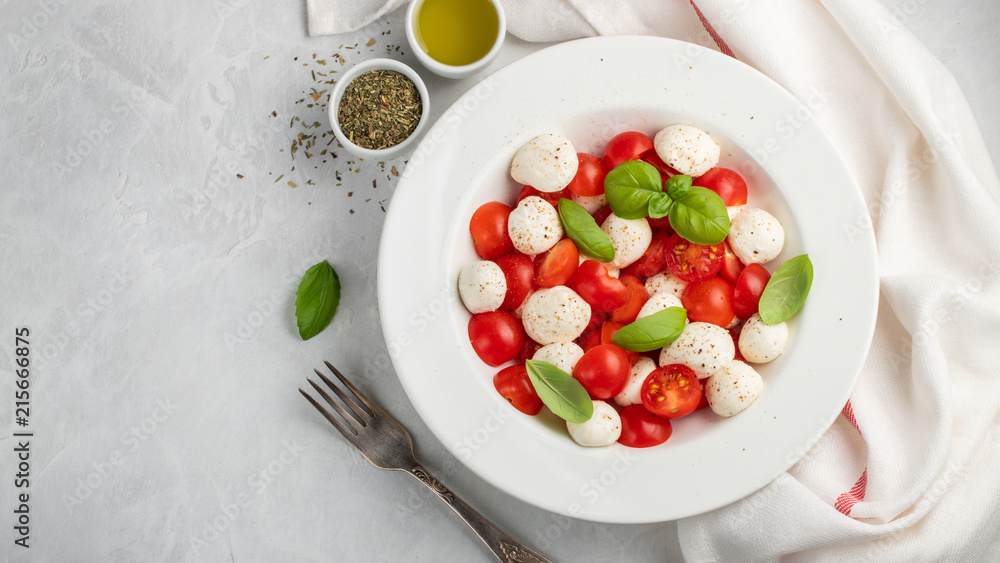 White plate of classic delicious caprese salad with ripe tomatoes, mozzarella and fresh basil leaves on gray background. copy space. Italian food. The concept of a healthy vegetarian diet. Top view White plate of classic delicious caprese salad with ripe tomatoes, mozzarella and fresh basil leaves on gray background. copy space. Italian food. The concept of a healthy vegetarian diet. Top view