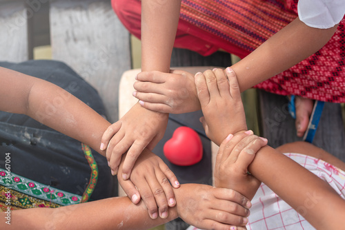 Young children hands assembly, hands join as a joyful, togetherness, friendship, and teamwork. Children playing as a team  with blurred red heart on hands circle outdoor.