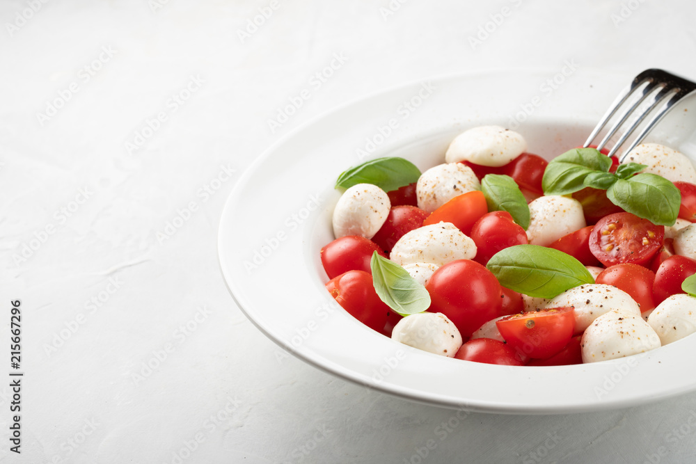 White plate of classic delicious caprese salad with ripe tomatoes, mozzarella and fresh basil leaves on gray background with copy space. Italian food. The concept of a healthy vegetarian diet White plate of classic delicious caprese salad with ripe tomatoes, mozzarella and fresh basil leaves on gray background with copy space. Italian food. The concept of a healthy vegetarian diet