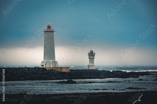 White lighthouse of Arkranes in natural bright light in Iceland with two houses near him surrounded by water and rocks. photo