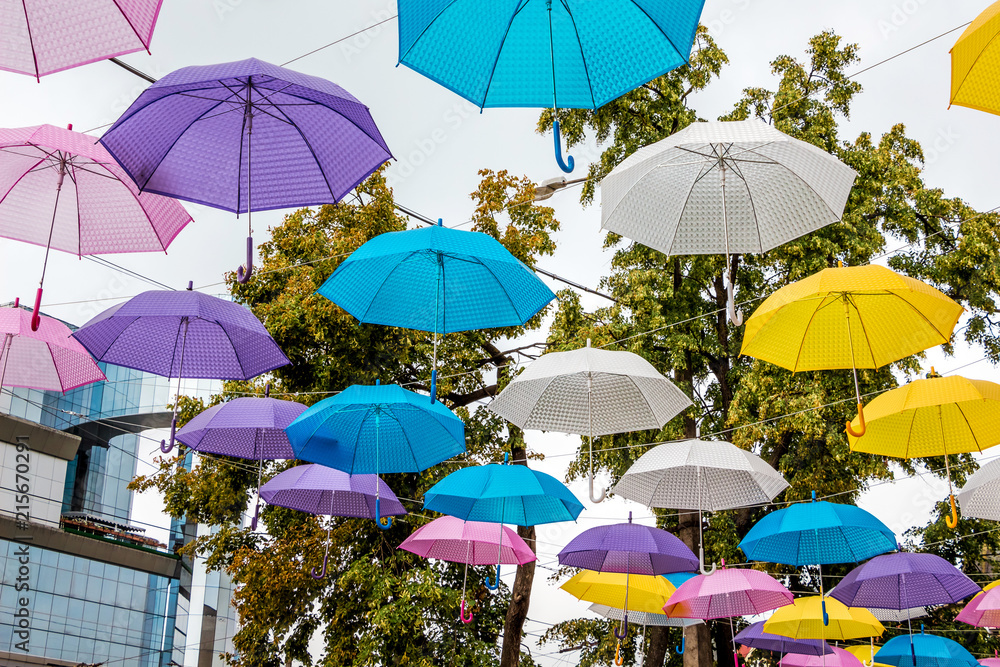 Multicolored umbrellas on the streets of the city on the background trees and modern buildings_