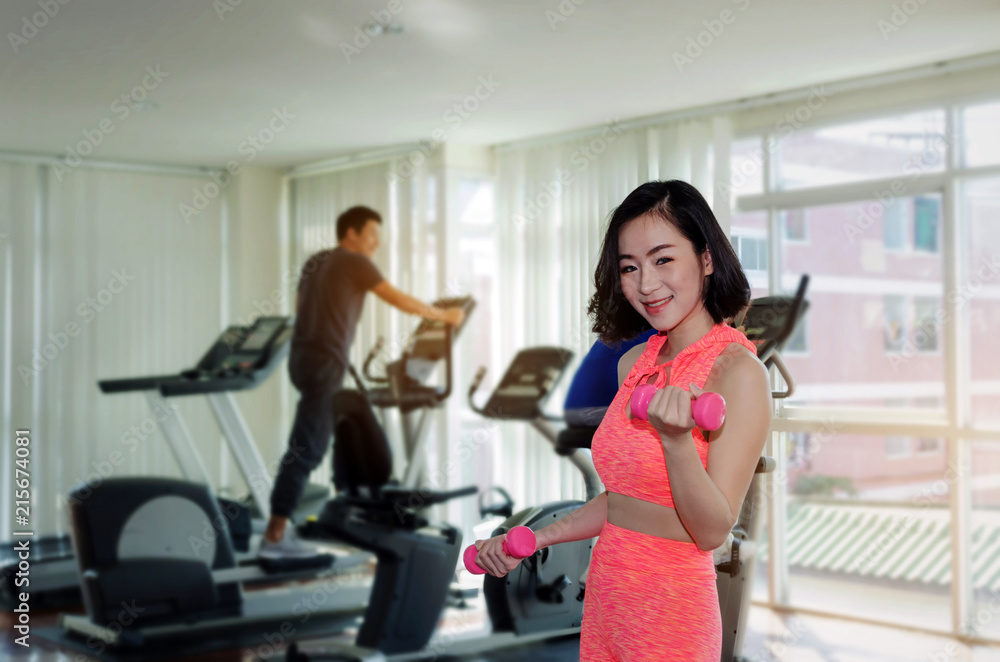 young asian pretty woman doing exercises with dumbbell at biceps in fitness gym with people background, bodybuilder, healthy lifestyle, exercise fitness, workout and sport training concept, soft focus young asian pretty woman doing exercises with dumbbell at biceps in fitness gym with people background, bodybuilder, healthy lifestyle, exercise fitness, workout and sport training concept, soft focus