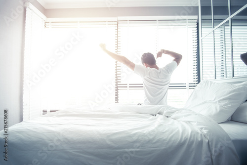 Man wake up and stretching on bed in morning with sunlight