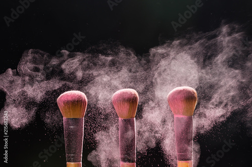 Mineral make up and objects concept - Three make up brushers in pink dust over dark background