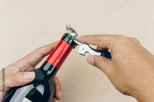 hand using a metal corkscrew knife to cut the foil capsule of the red wine bottle