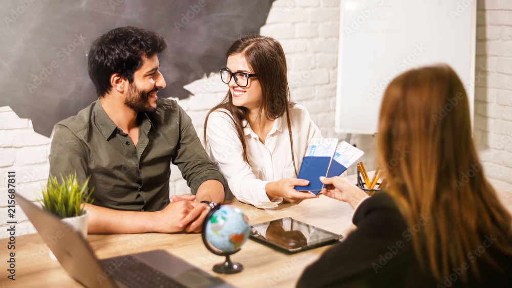 Young lovely couple sitting with manager at the travel agency office prepairing for a summer vacation Young lovely couple sitting with manager at the travel agency office prepairing for a summer vacation
