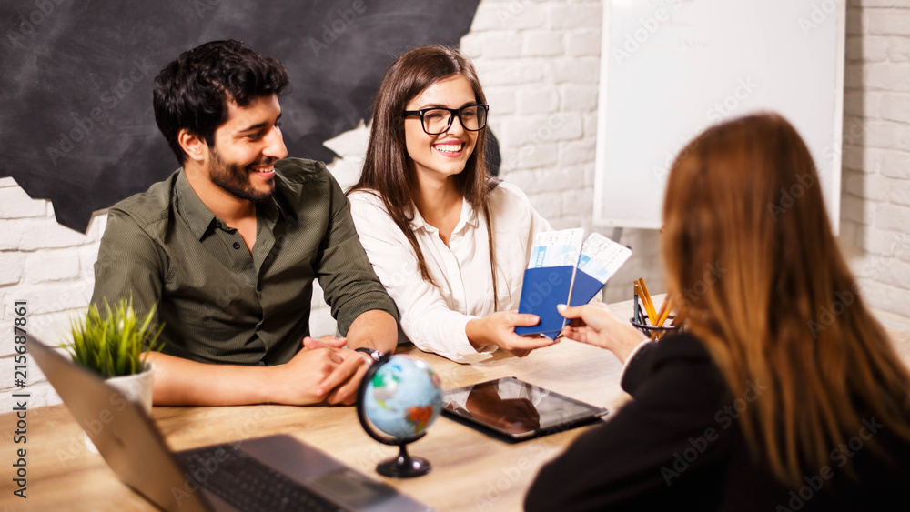 Young cute couple choosing a trip with agent sitting at the travel agency office with world map on the background Young cute couple choosing a trip with agent sitting at the travel agency office with world map on the background
