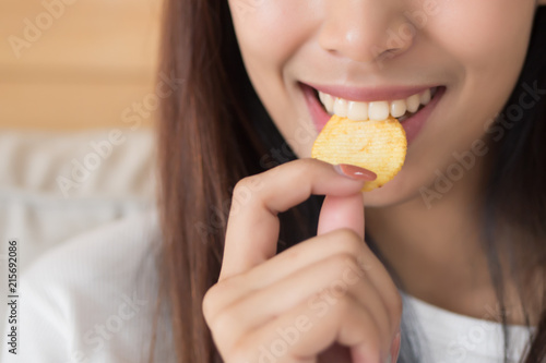 Obraz na płótnie happy, smiling woman eating potato chips or crispy fried potato; unhealthy food