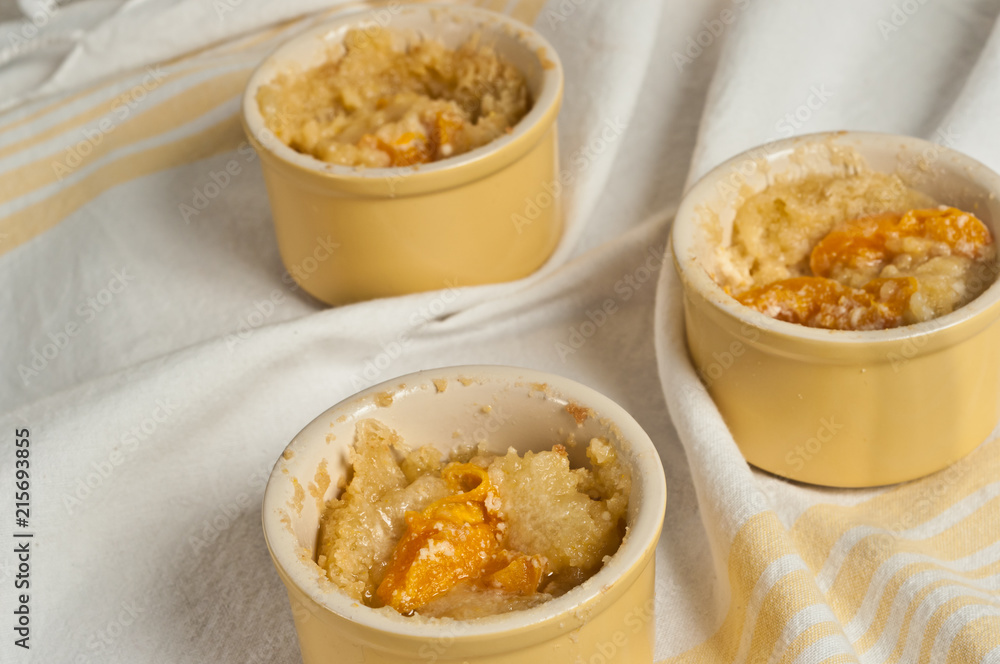 Top view, medium distance of three freshly baked, homemade apricot sour cream crumble in yellow baking cups cooling on a yellow and white striped cloth Top view, medium distance of three freshly baked, homemade apricot sour cream crumble in yellow baking cups cooling on a yellow and white striped cloth