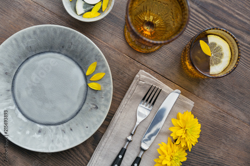 Rustic table setting with linen napkin  cutlery  ceramic plates  yellow glasses and yellow flowers