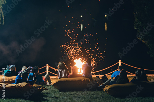 Photos Group of people near camp fire with campfire song and campfire meals playing campfire games and eating campfire grill, telling campfire stories near the fire with wood, flames in the nature at night