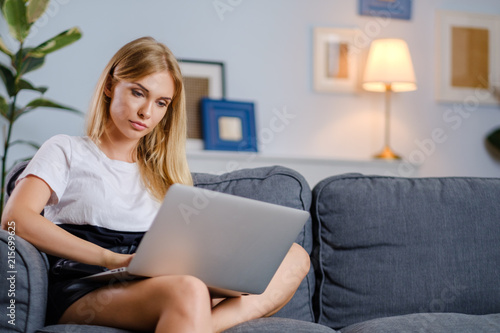 Pretty woman using laptop sitting on cosy sofa