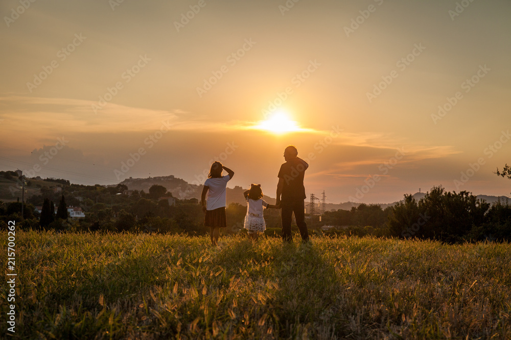 Φωτογραφία Grandfather and his children silhouette look to the horizon in the sunset light