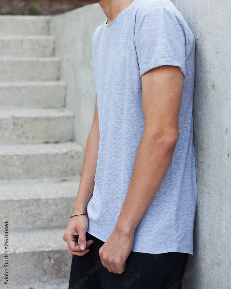 Youth fashion. A man in a gray fashionable T-shirt posing on a gray stone background in the summer evening. Cover. Part of the body.