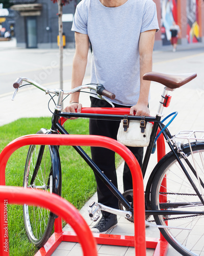 Youth fashion. Portrait of a sporty hipster man in a gray fashionable T-shirt posing with a tricycle bike on a street in the summer evening. Cover. Part of the body.