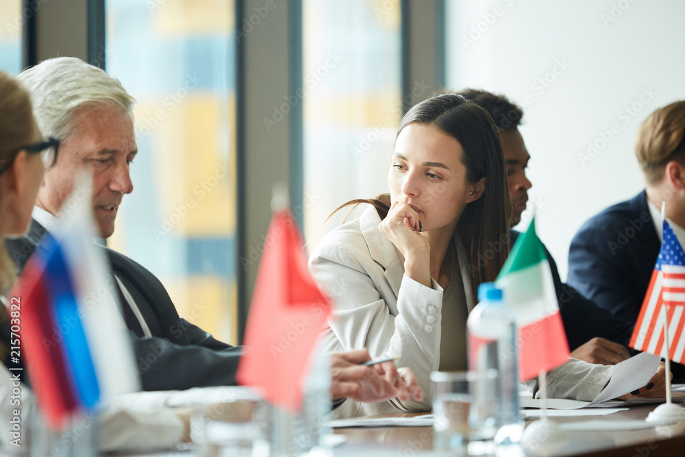 Fototapeta premium Pensive attractive young woman leaning on hand and listening to country representative at government meeting