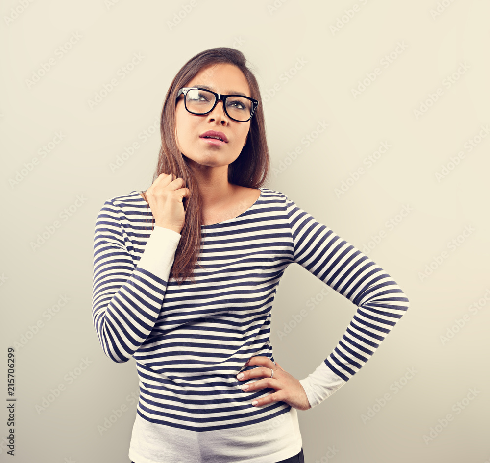 Beautiful business serious woman in glasses looking up and scratched the head with thinking look on empty space background. Toned closeup portrait