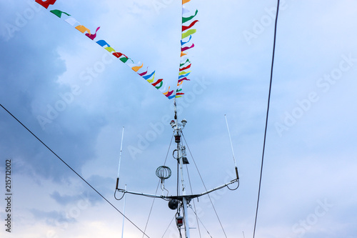 mast ship with multi-colored ribbons flags on the background of sky and clouds