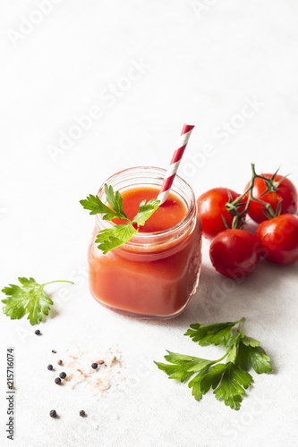 Tomato juice with fresh tomatoes, parsley, sea salt and pepper on light grey background. Vegetable drink.