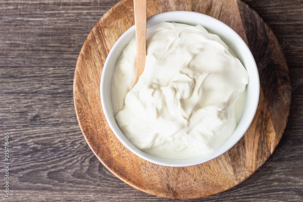 White bowl with sour cream or homemade yogurt on a wooden tray, top view. White bowl with sour cream or homemade yogurt on a wooden tray, top view.