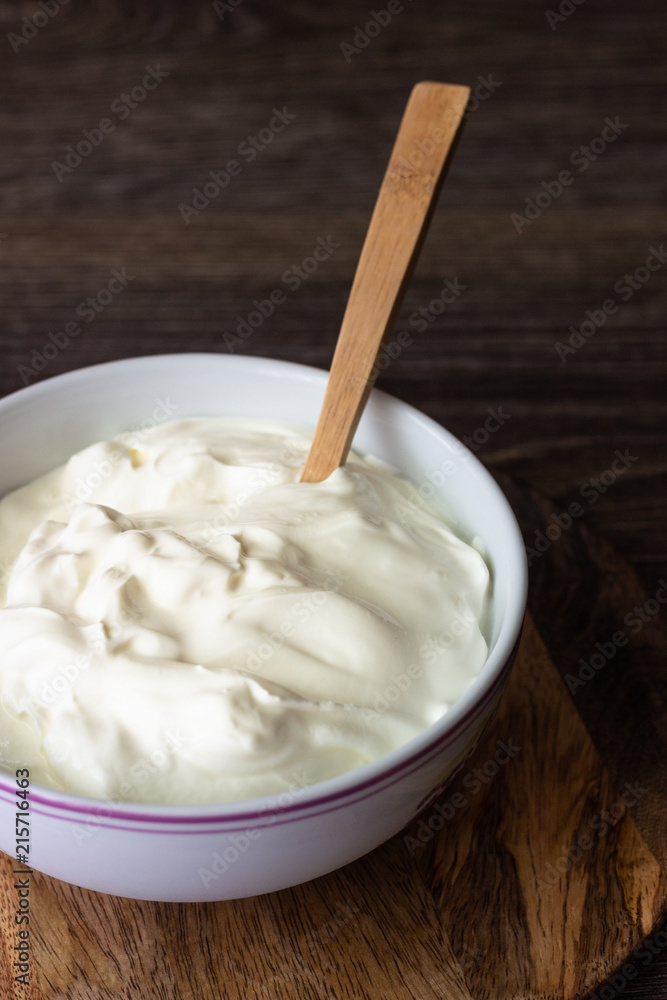 White bowl with sour cream or homemade yogurt on a wooden tray, top view. White bowl with sour cream or homemade yogurt on a wooden tray, top view.