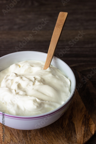 White bowl with sour cream or homemade yogurt on a wooden tray, top view.