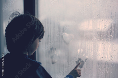 Little boy, leaving finger prints and drawing hearts on a window