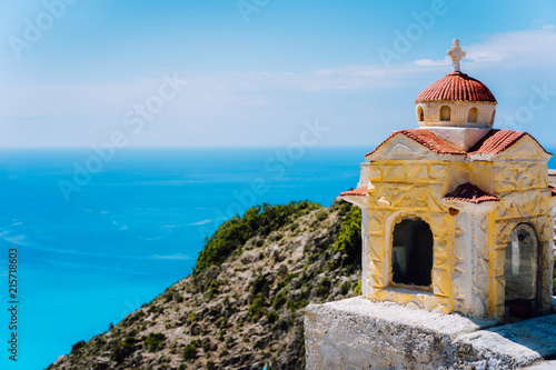Small orange colored Hellenic shrine Proskinitari on the cliff edge with defocused sea view in the background photo