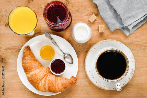 Croissant, cup of coffee, cream, orange juice, honey and jam on wooden table. Breakfast in cafe, hotel, continental breakfast or coffee break concept