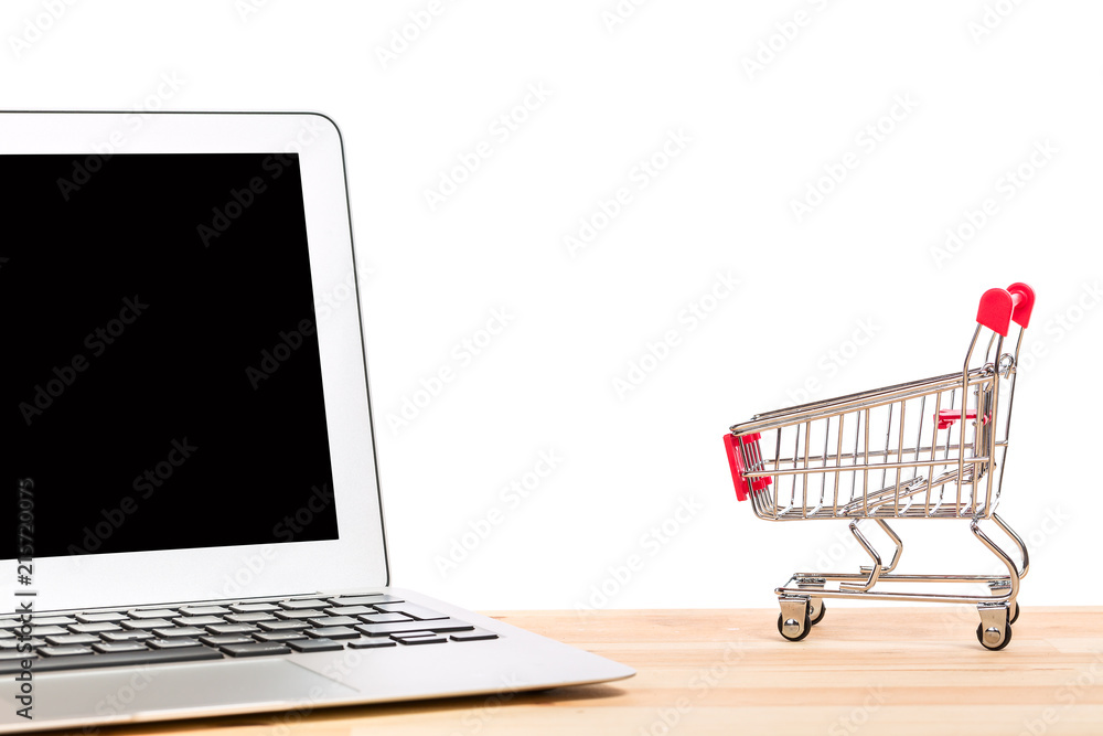Red shopping cart near laptop isolated on white background. Online internet shopping concept.