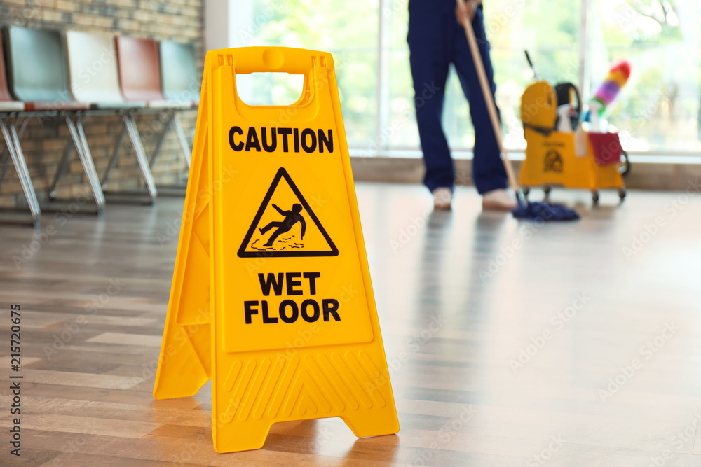 Safety sign with phrase Caution wet floor and blurred cleaner on background - obrazy, fototapety, plakaty 