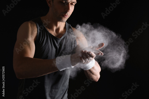 Young man applying chalk powder on hands against dark background