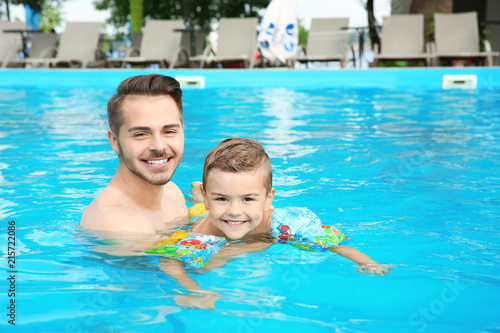Father teaching son to swim with inflatable sleeves in pool on sunny day © New Africa