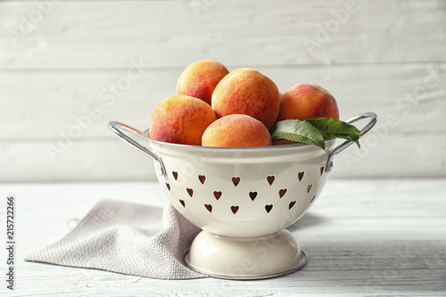 Colander with delicious ripe peaches on table