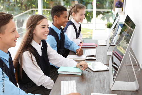 Obraz na plátně Teenage students in stylish school uniform at desks with computers