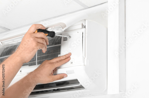 Male technician fixing modern air conditioner indoors