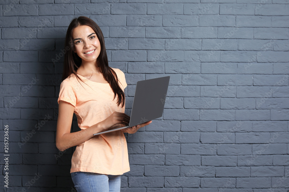 Young woman with modern laptop on brick wall background Young woman with modern laptop on brick wall background