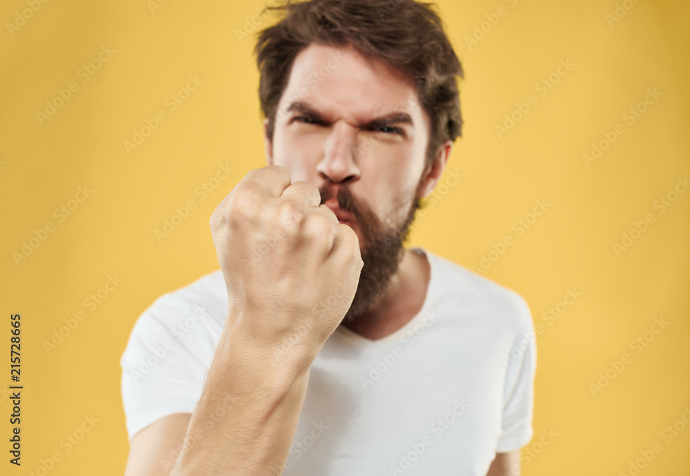 angry man with a beard shows a fist on a yellow background